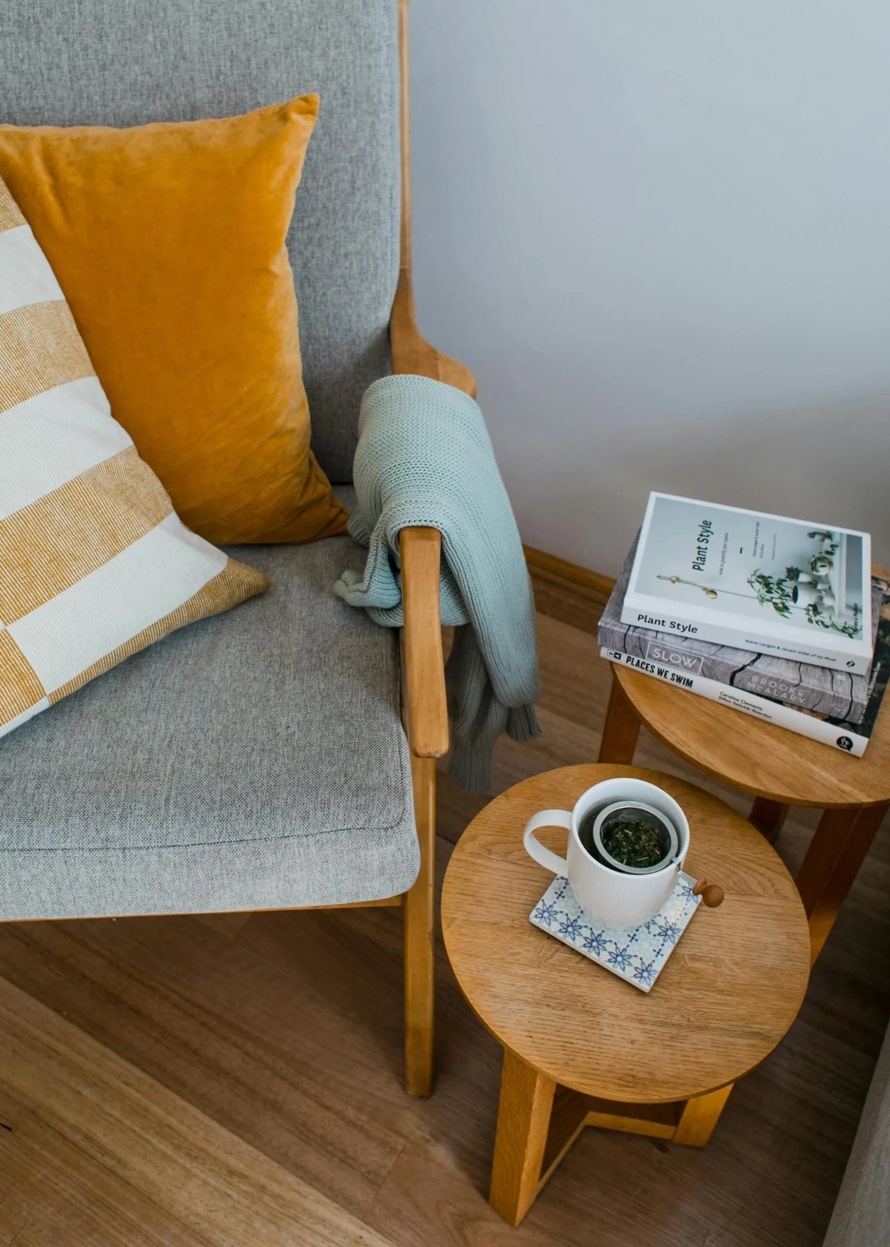 Comfortable armchair with colourful cushions next to wooden side tables with books and a cup of tea in a living room, seen from above
