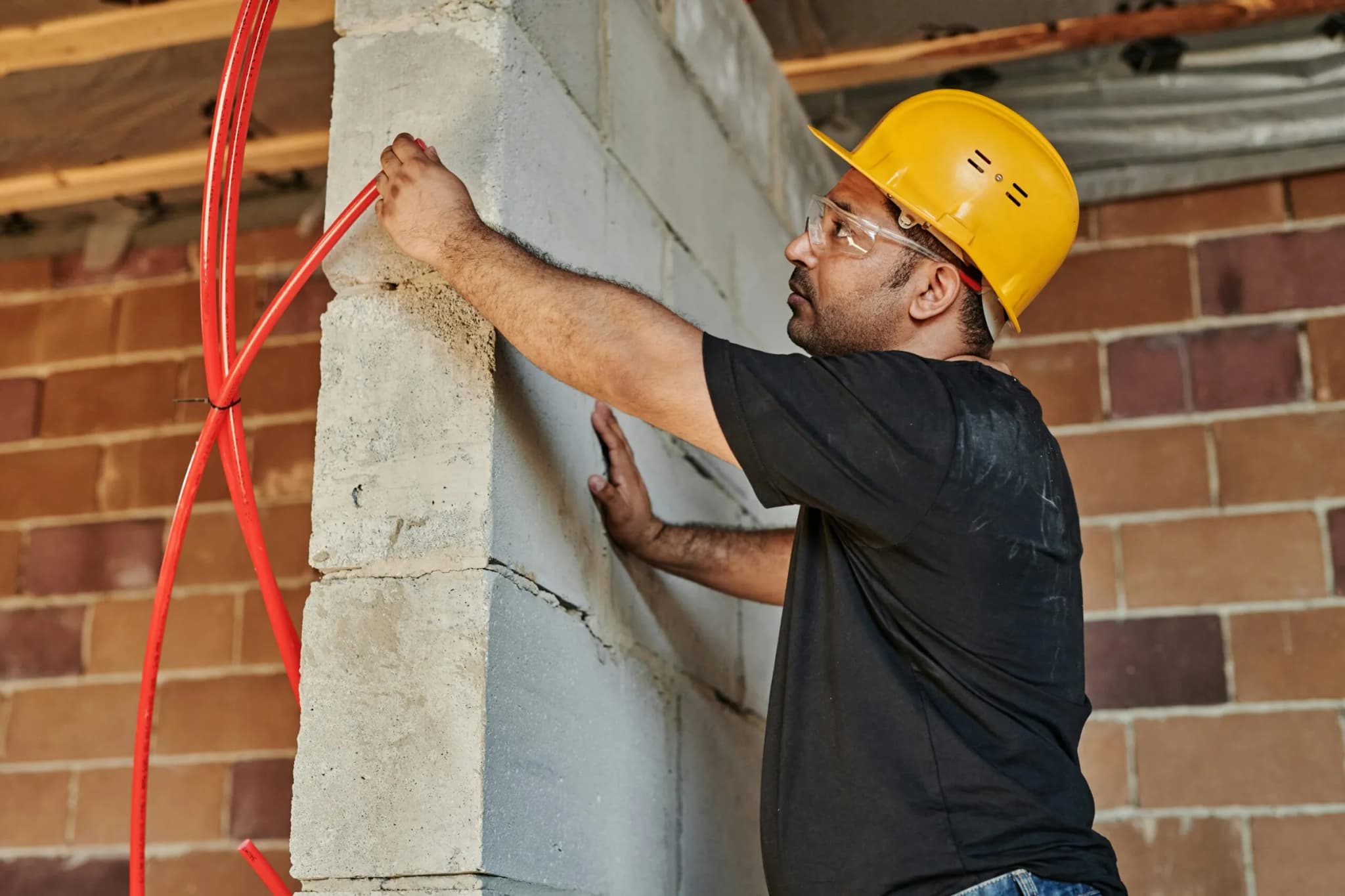 Tradesman in a hard hat pulling cables through a wall