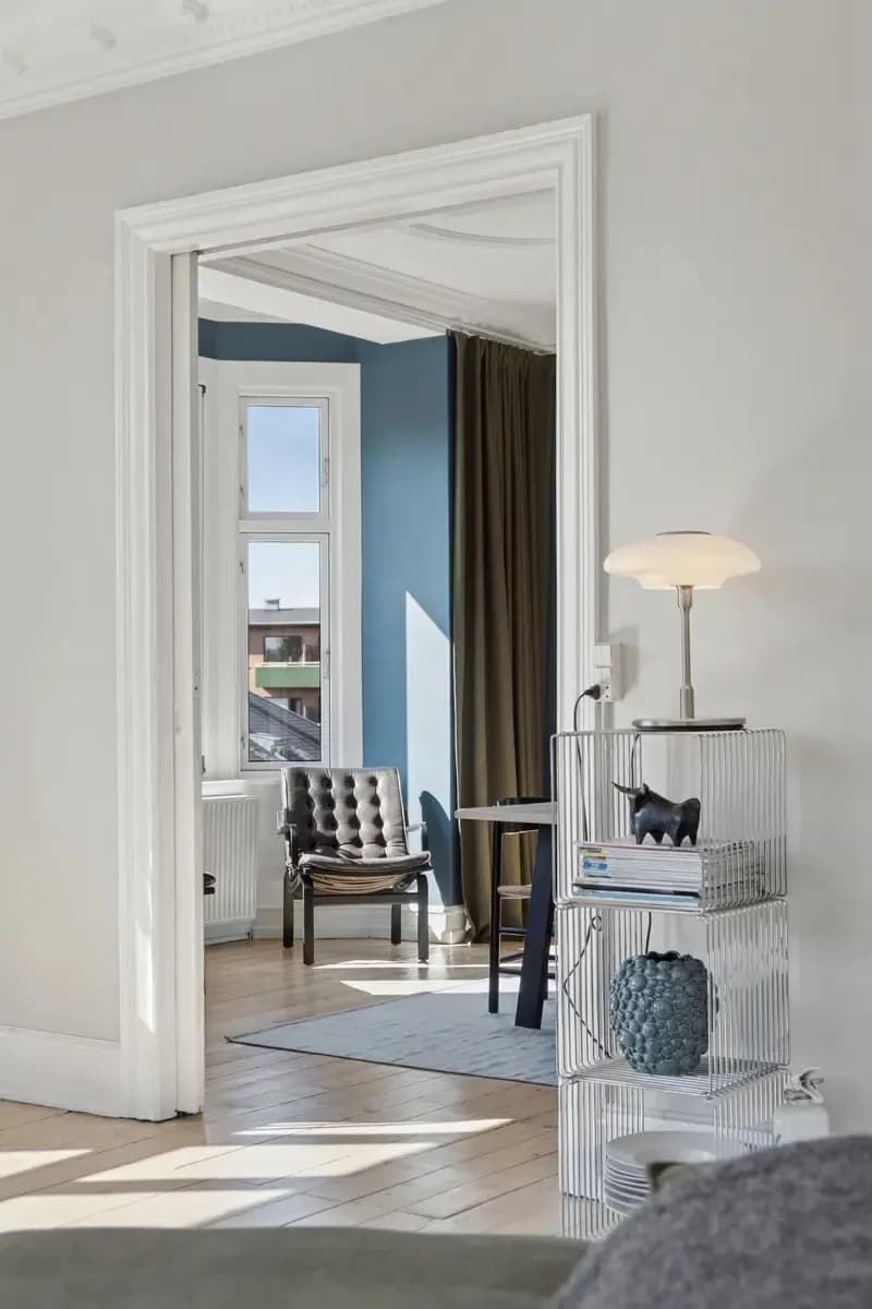 Living room with blue walls, an armchair and a table lamp, seen through a white door frame