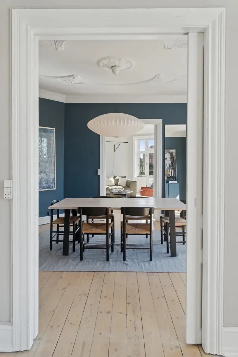 Dining room with a long table, chairs and a pendant lamp, seen through open doors