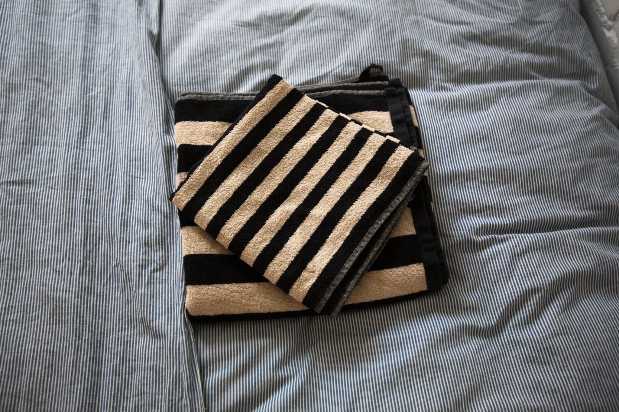 Striped towels on a made bed with blue-striped linen