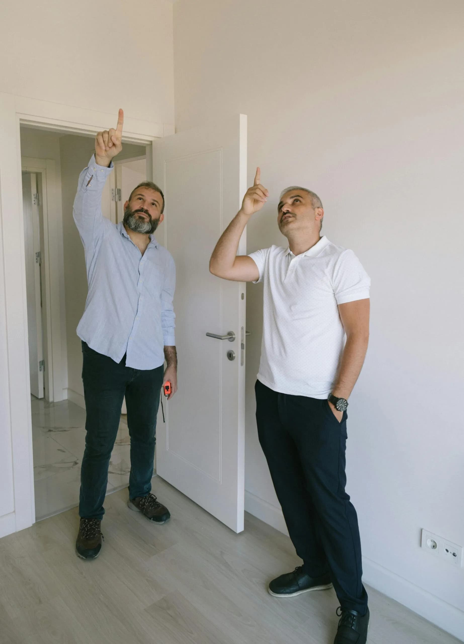 Two men inspect the ceiling of an empty room during an inspection