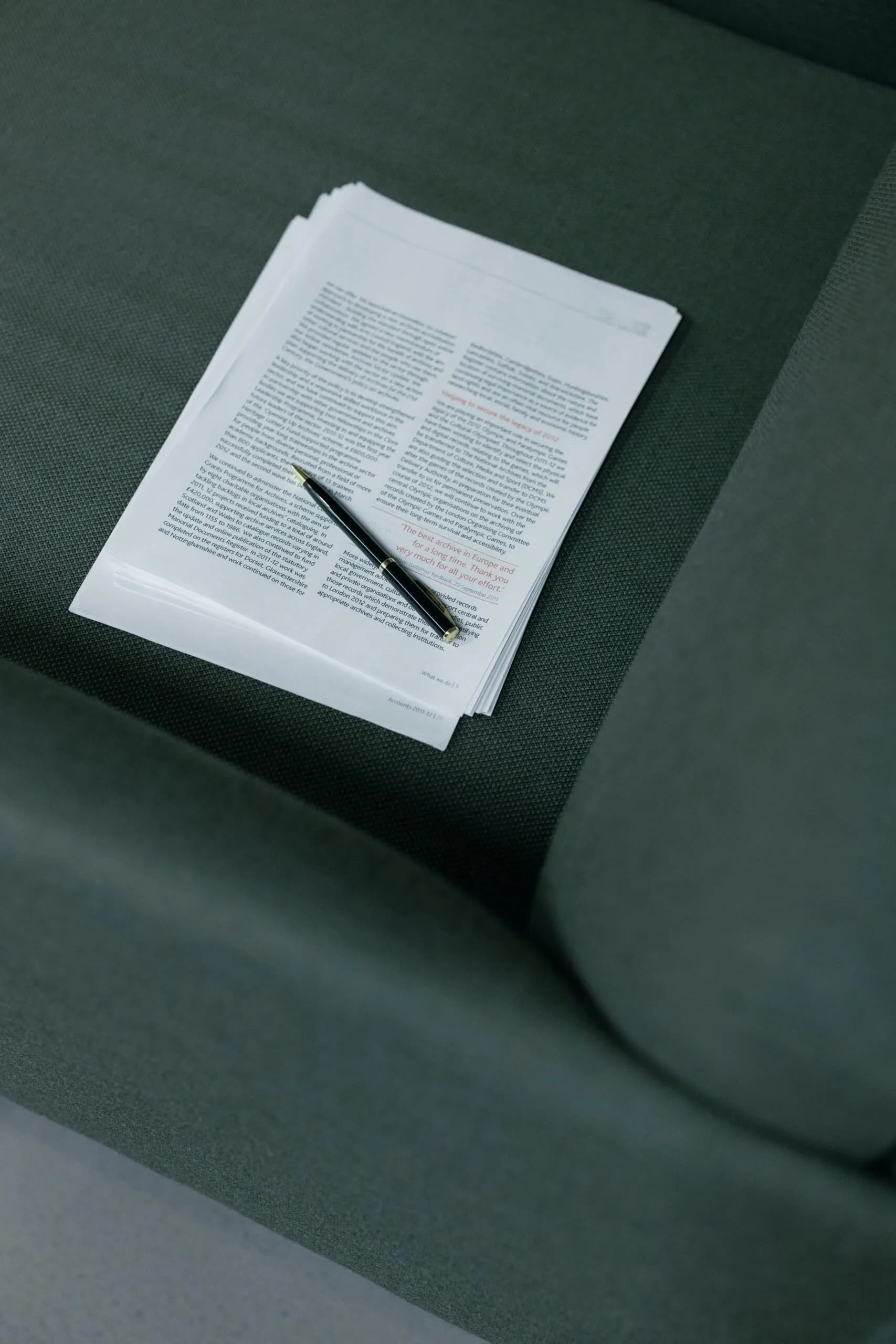 A printed contract and a pen on a dark green sofa