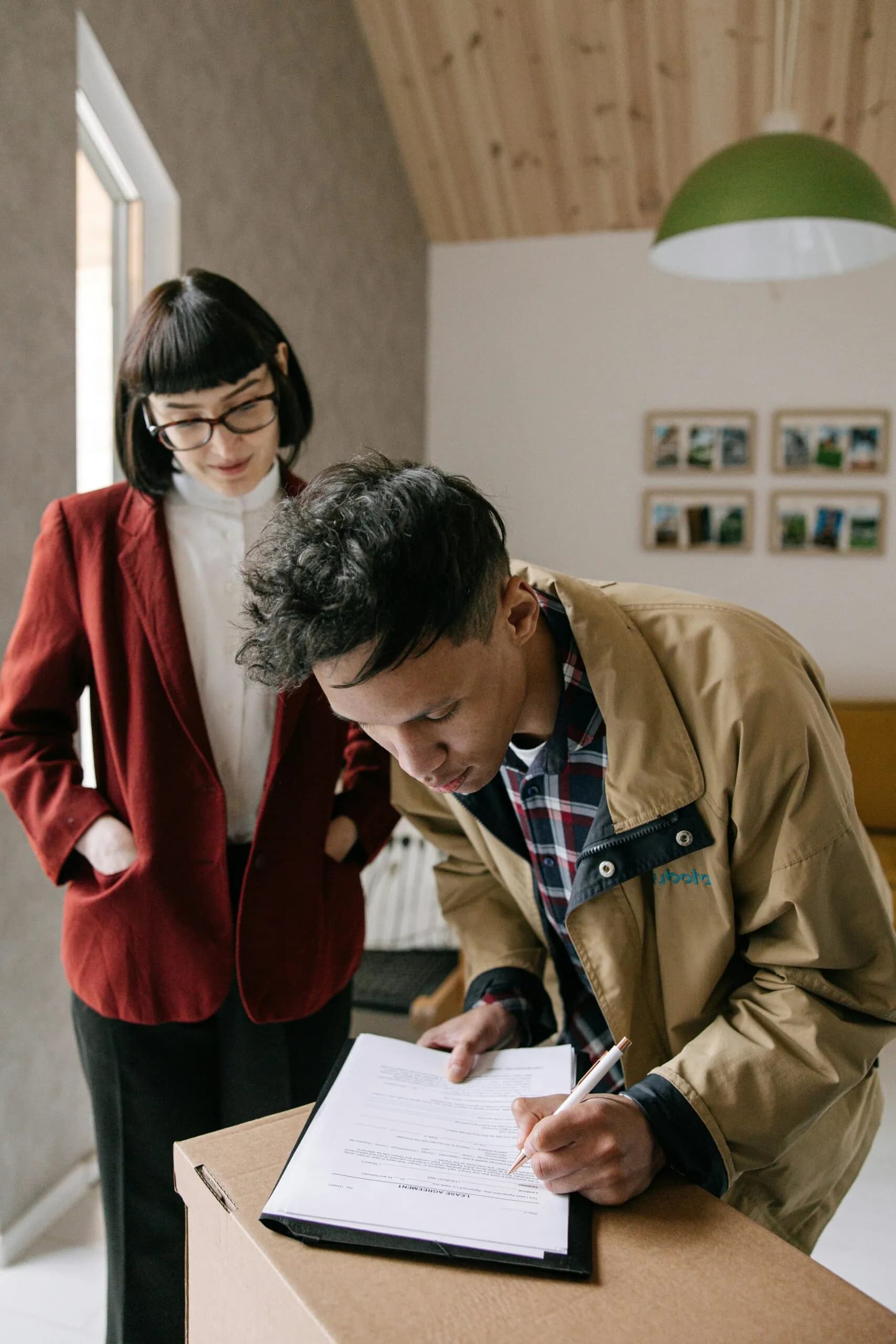 A young man signs a document on a moving box while a woman looks on