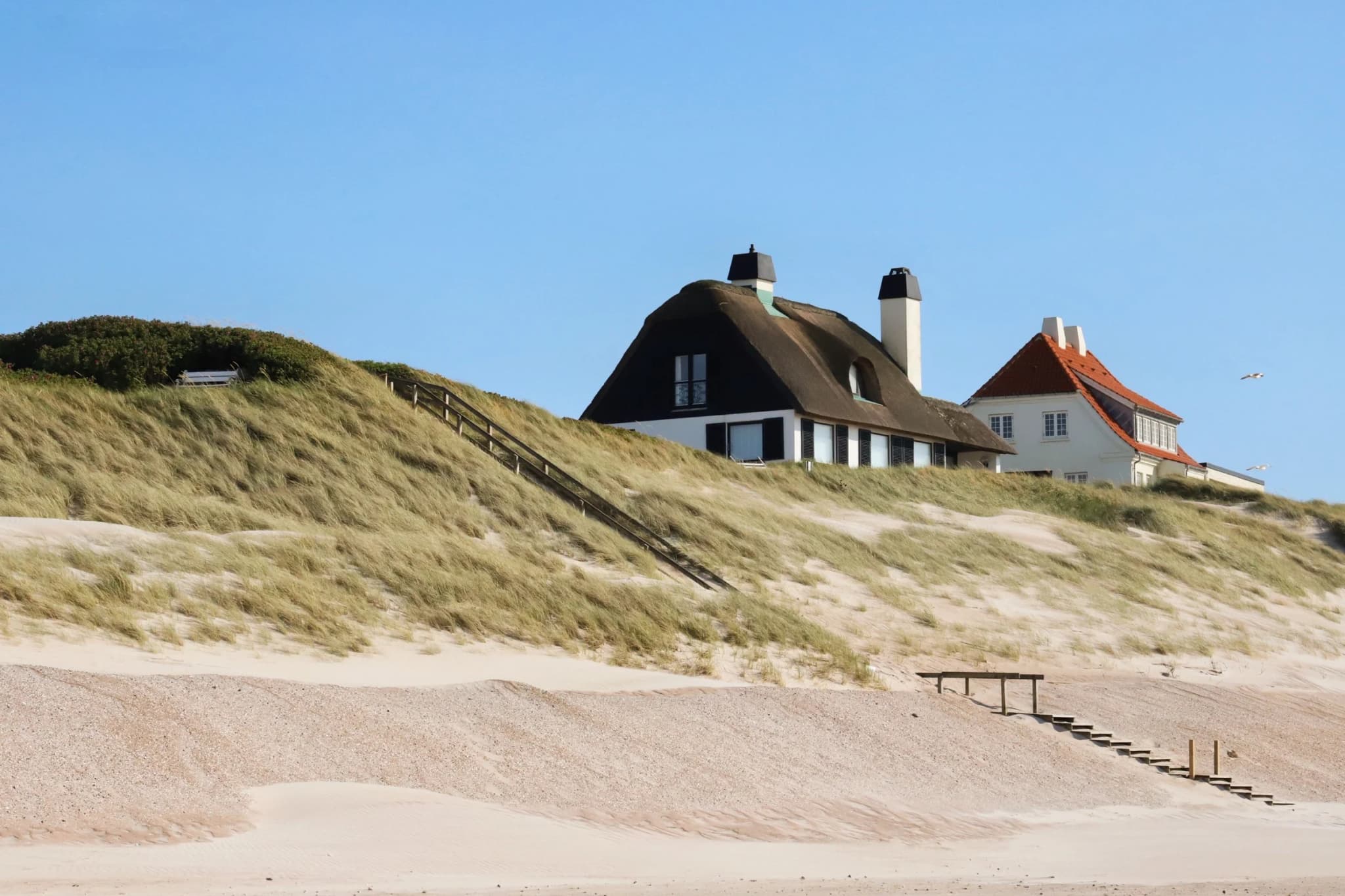 Stråtækte sommerhuse på en klit med trappe ned til stranden