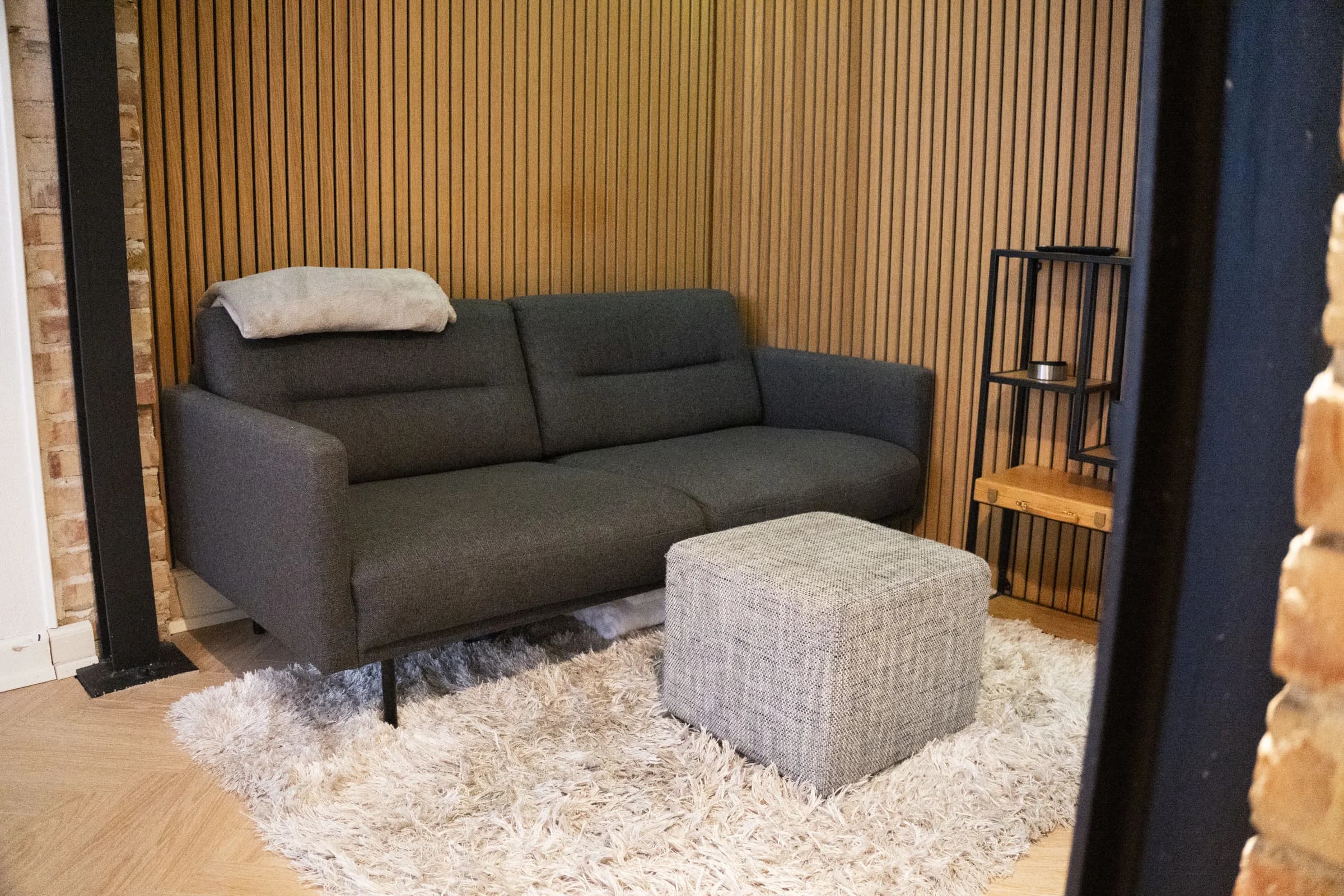 Stue med træbeklædt væg og grå sofa