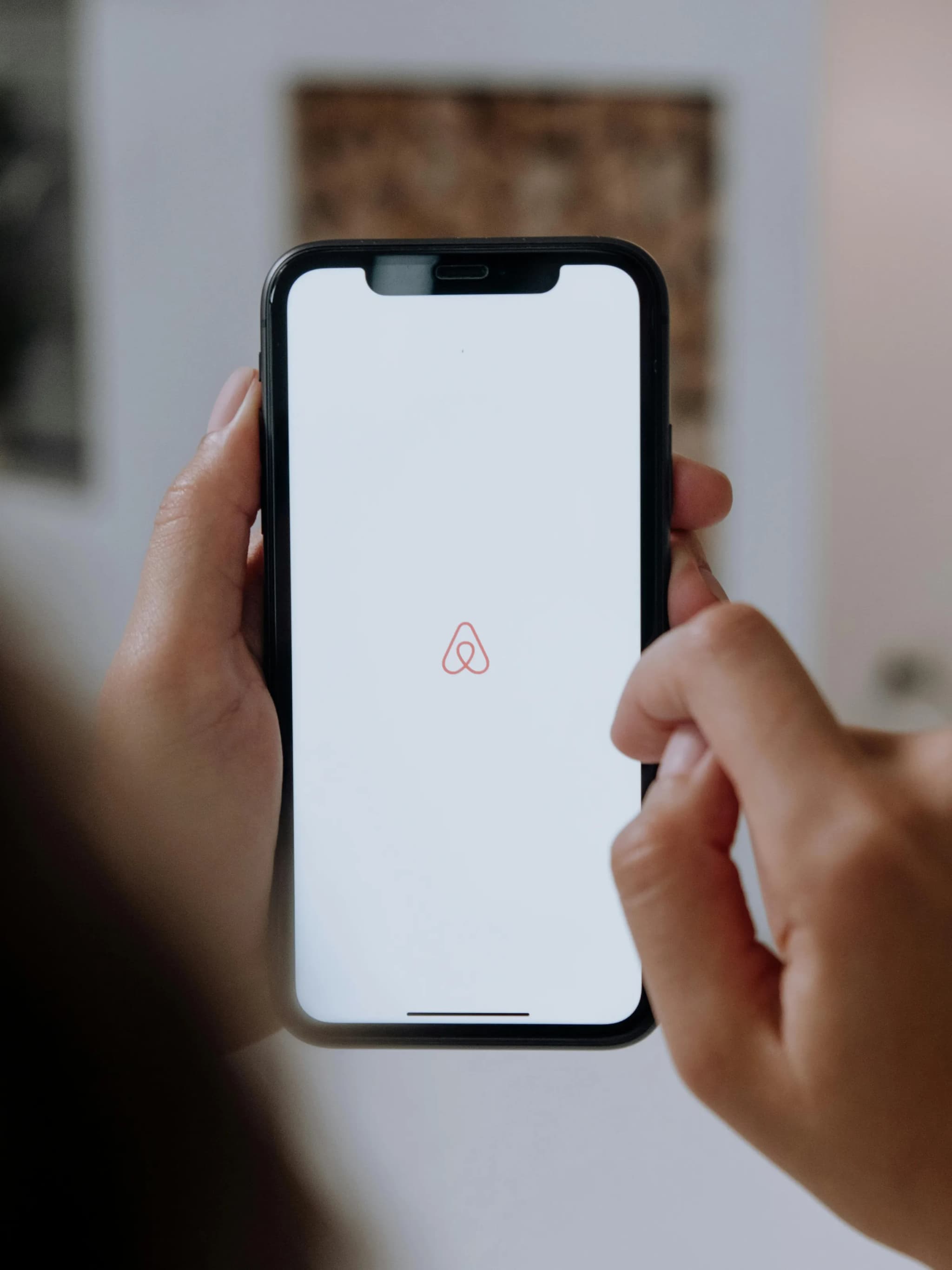 Close-up of hands holding a smartphone with Airbnb app logo on the screen indoors, highlighting modern technology.