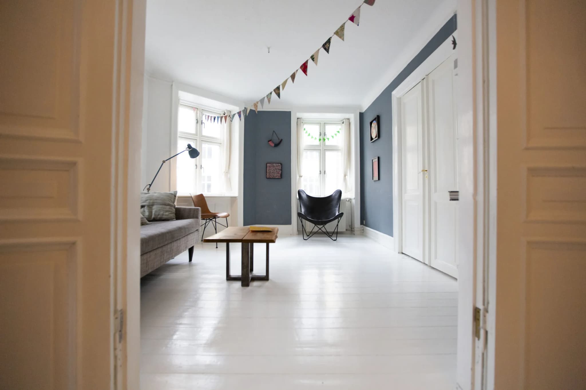 Open double doors into a bright living room with a white-painted plank floor