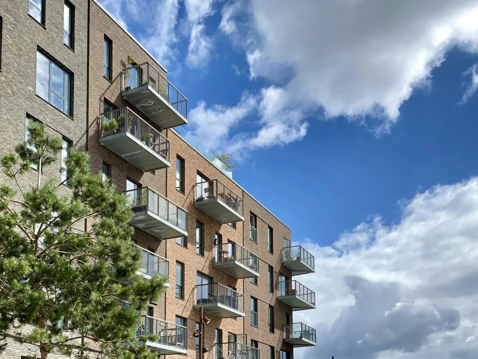 Nybygget murstensejendom med altaner i Nordhavn set nedefra mod en blå himmel