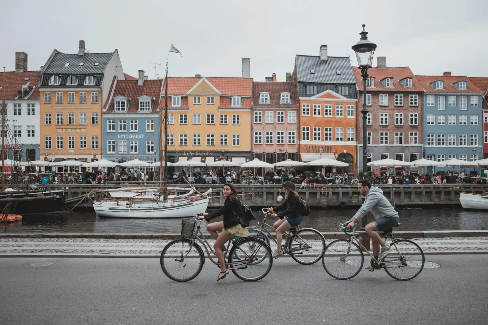 Turister på cykel langs Nyhavns kanal med de farvede husfacader i baggrunden