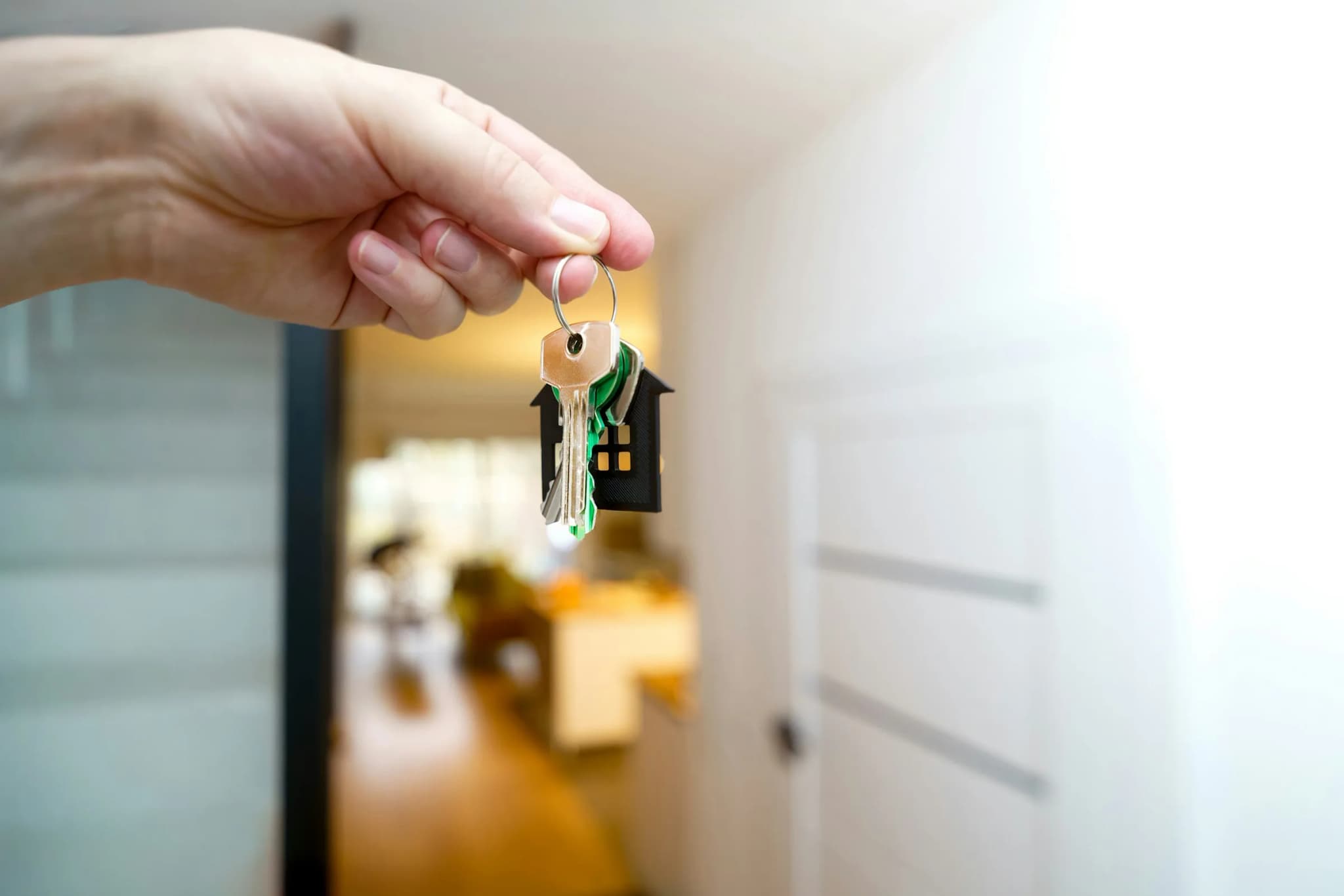 En hånd rækker en nøgle med et hus-formet nøglebrik frem i en lys entré