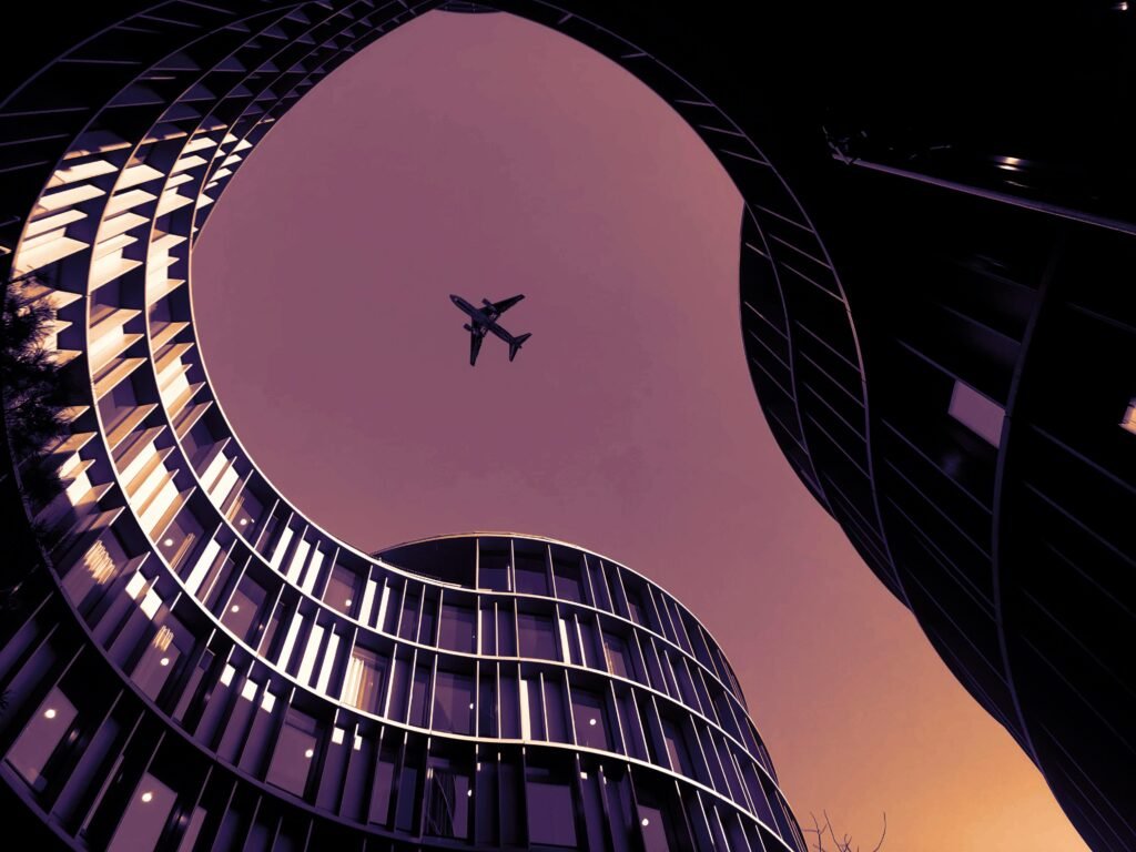 Low-angle shot of airplane over modern skyscrapers in Copenhagen at dusk.