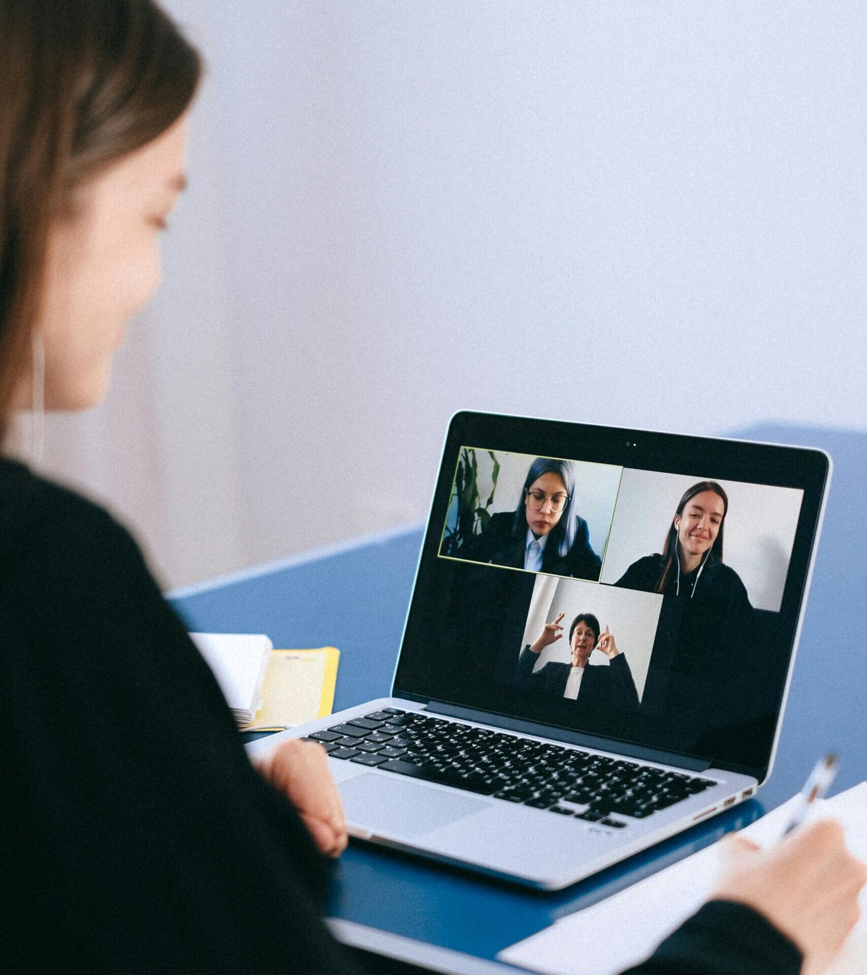 A woman participates in a virtual meeting with colleagues via video call on a laptop.