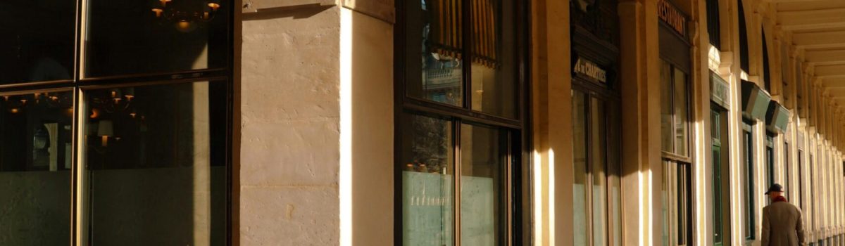 Sunlit corridor of Paris' Palais Royal highlighting classic architecture.
