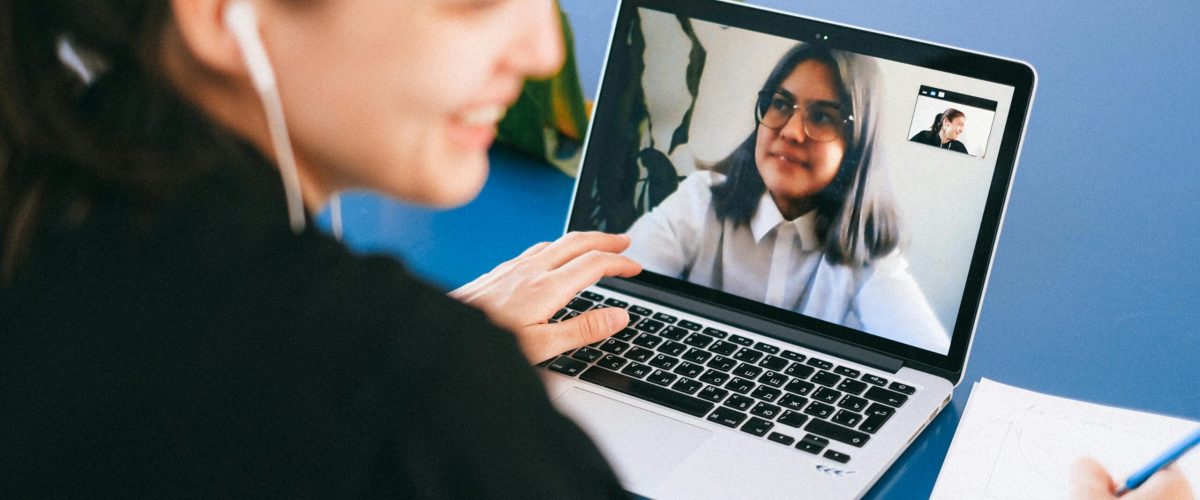 Woman having a video conference on a laptop, smiling and taking notes.