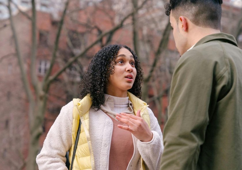 From below of ethnic female with short curly hair standing and arguing with boyfriend on street in daylight